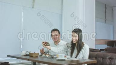 快乐的年轻夫妇在餐厅用智能手机端着食物